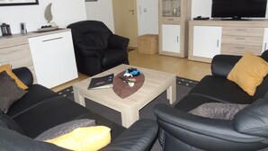 Een moderne woonkamer met een zwarte leren bank, een salontafel, een televisie en een kast.