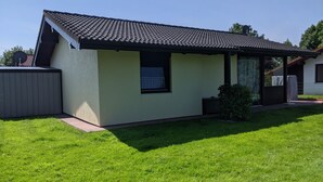 Een klein, laag huis met een pannendak, een klein raam en een verzorgd gazon.
