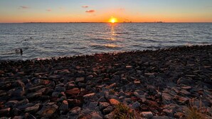 Uma costa rochosa ao pôr do sol, com o sol se pondo sobre a água.