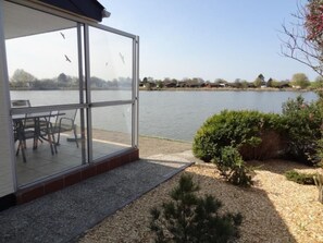Um alpendre envidraçado com uma mesa e cadeiras, com vista para um lago e casas ao longe.