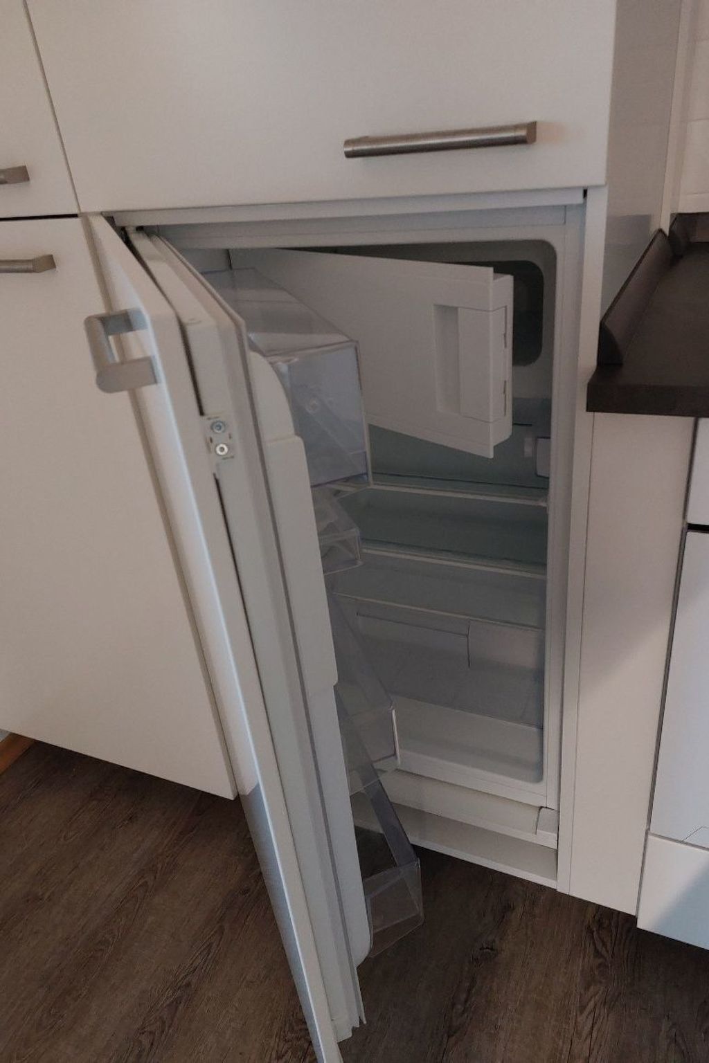 A kitchen with a white refrigerator, a wooden floor, and a white countertop.