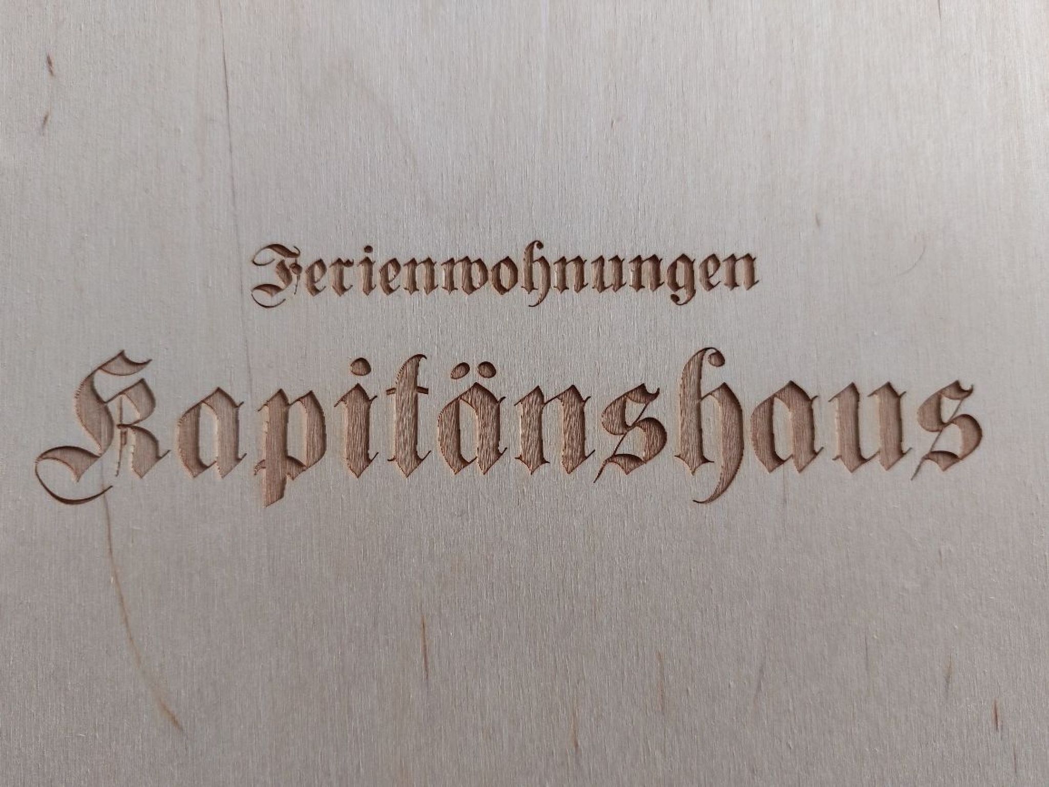 Eingravierter Text auf einer Holzfläche mit der Aufschrift 'Ferienwohnungen Kapilönshaus'.