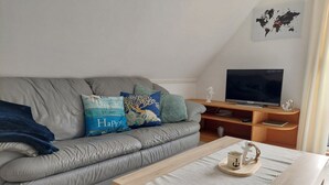 Un salon moderne avec un canapé gris, une table basse en bois et un téléviseur posé sur un meuble en bois.