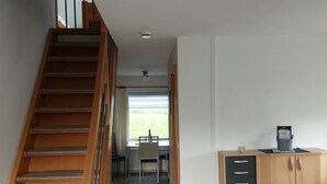 Un intérieur moderne avec un escalier en bois, un coin repas et une petite cuisine.