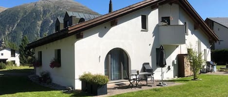 Um edifício branco com telhado marrom, porta frontal e pequeno pátio com mobiliário de exterior.