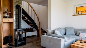 Een gezellige woonkamer met een grijze bank, houten vloeren, een houten trap en een open haard.