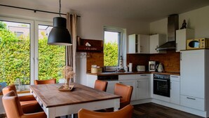 Een moderne keuken met witte kasten, een houten aanrecht en een eethoek met een houten tafel en oranje stoelen.