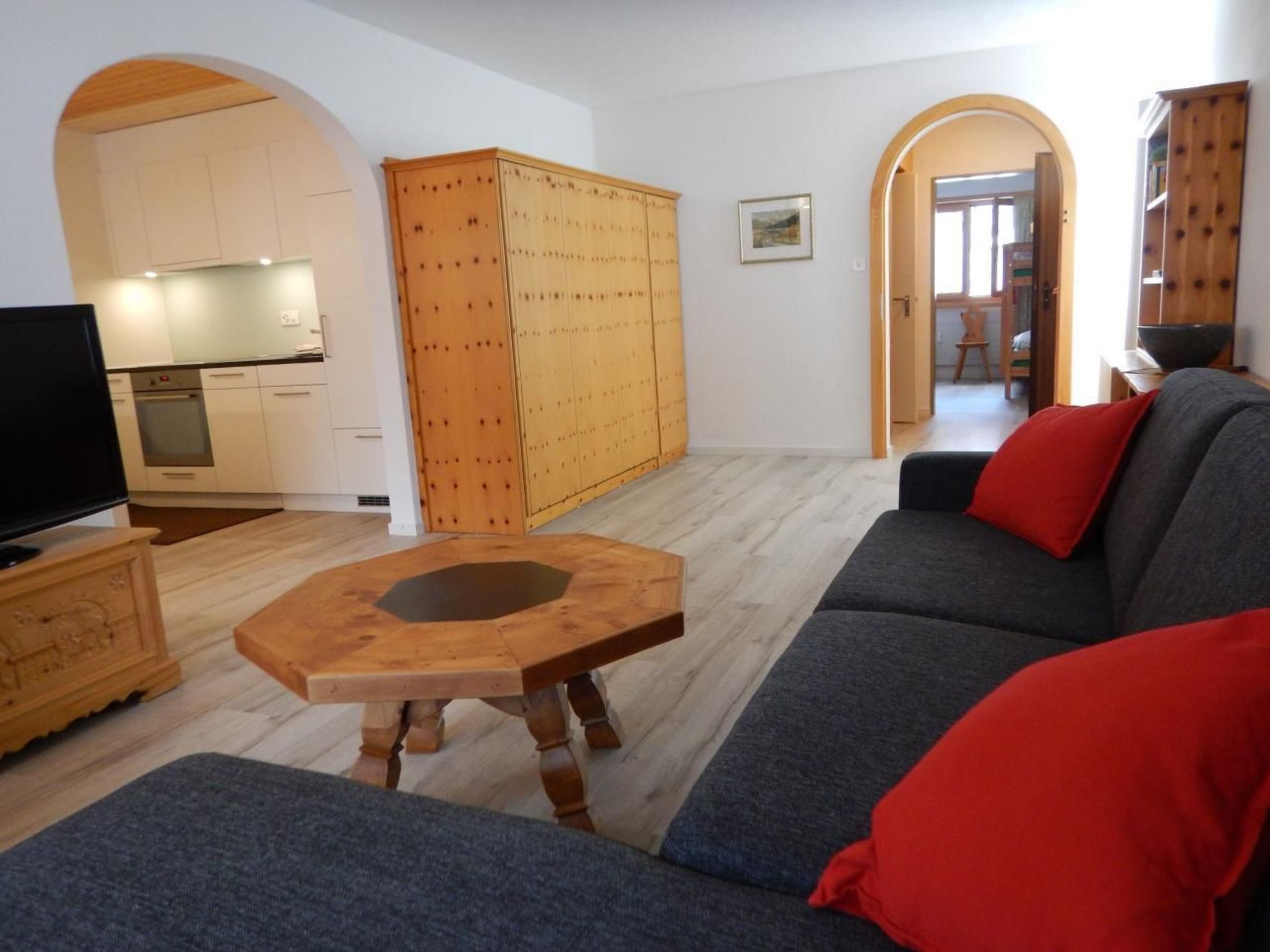 Un salon moderne avec un canapé gris, une table basse en bois et un téléviseur posé sur un meuble en bois.