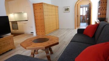 Un salon moderne avec un canapé gris, une table basse en bois et un téléviseur posé sur un meuble en bois.