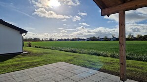 En uteplats med utsikt över en grön äng och hus i fjärran, under en delvis molnig himmel.