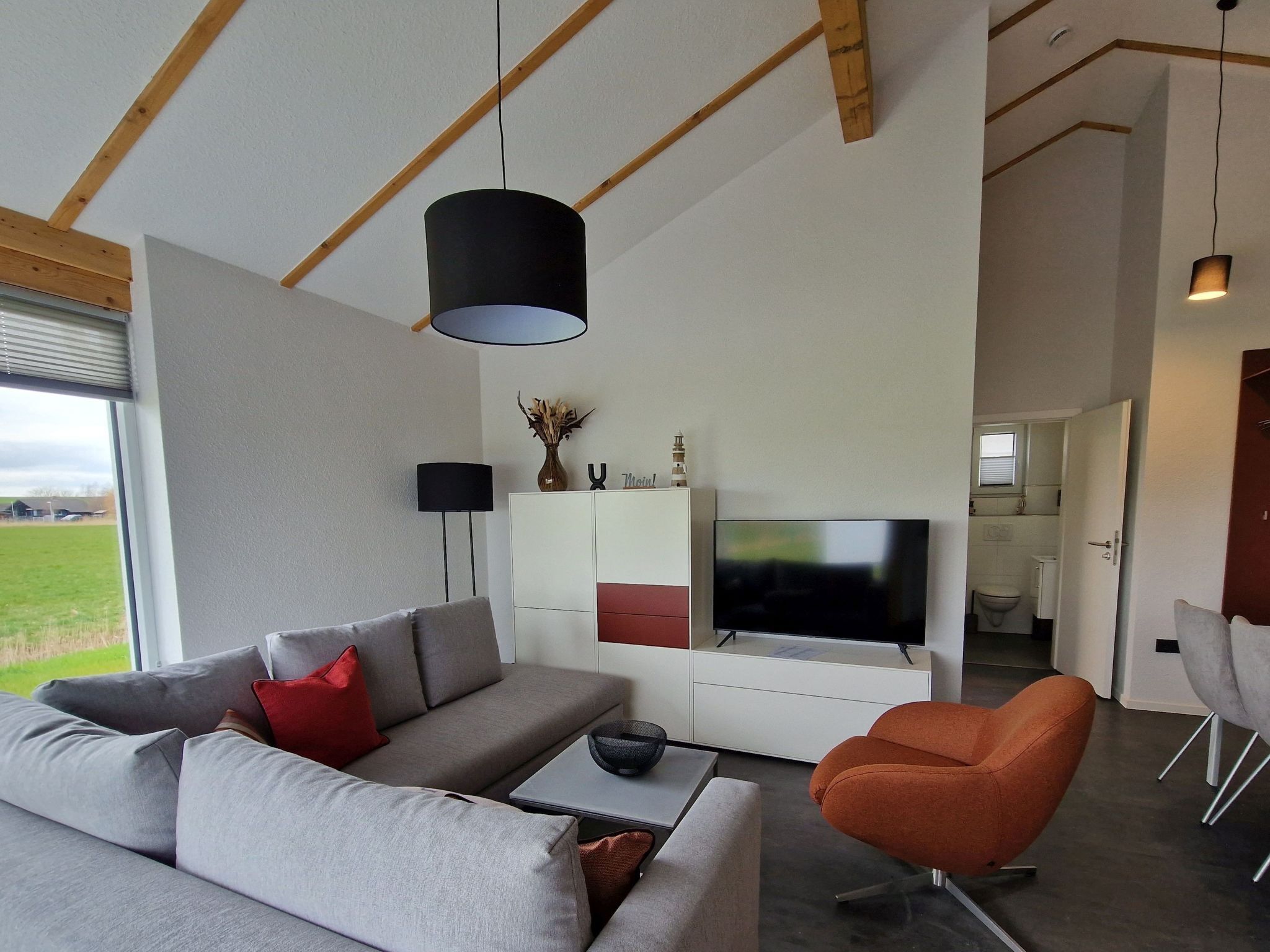 A modern living room with a grey sofa, an orange armchair, a flat-screen TV, and a wooden ceiling.