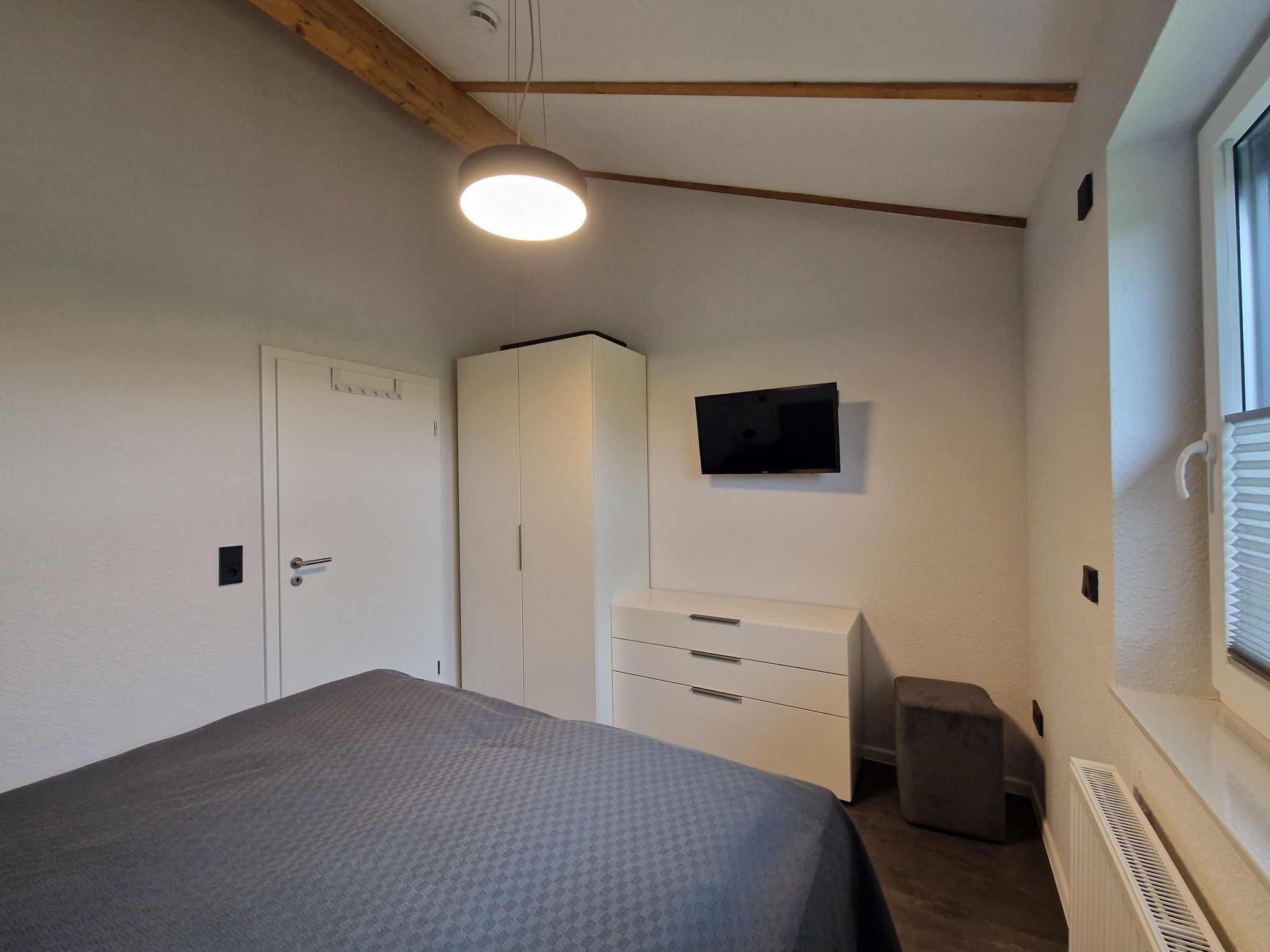 Een slaapkamer met een bed, een kledingkast, een televisie en een radiator.