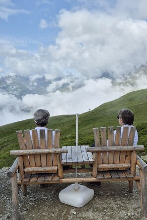 Two wooden Adirondack chairs facing a grassy hill with a mountain in the background. - Tscheppa B by Interhome (Camischolas)