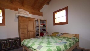A bedroom with a wooden bed, a wardrobe, a shelf with folded clothes, and a window. - Tscheppa B by Interhome (Camischolas)