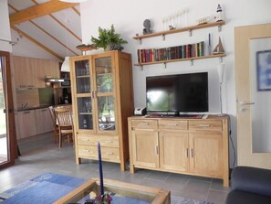 Ett modernt vardagsrum med en TV, träskåp, en bokhylla och en matplats.