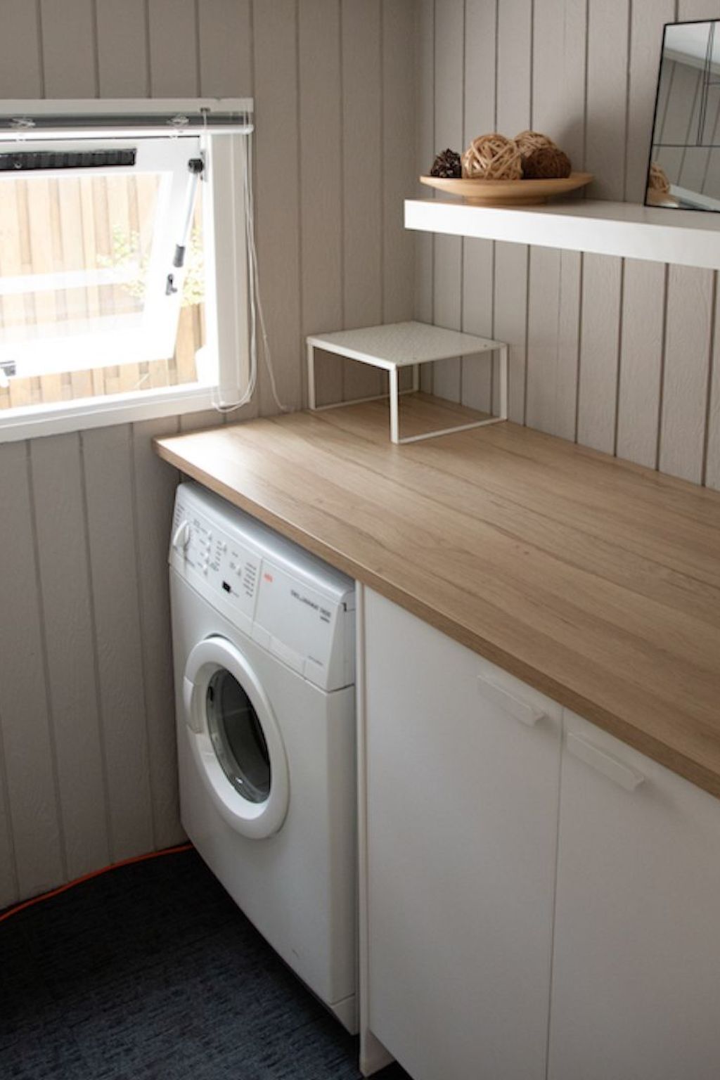 A compact laundry area with a washing machine, a drying rack, and a shelf with decorative items.