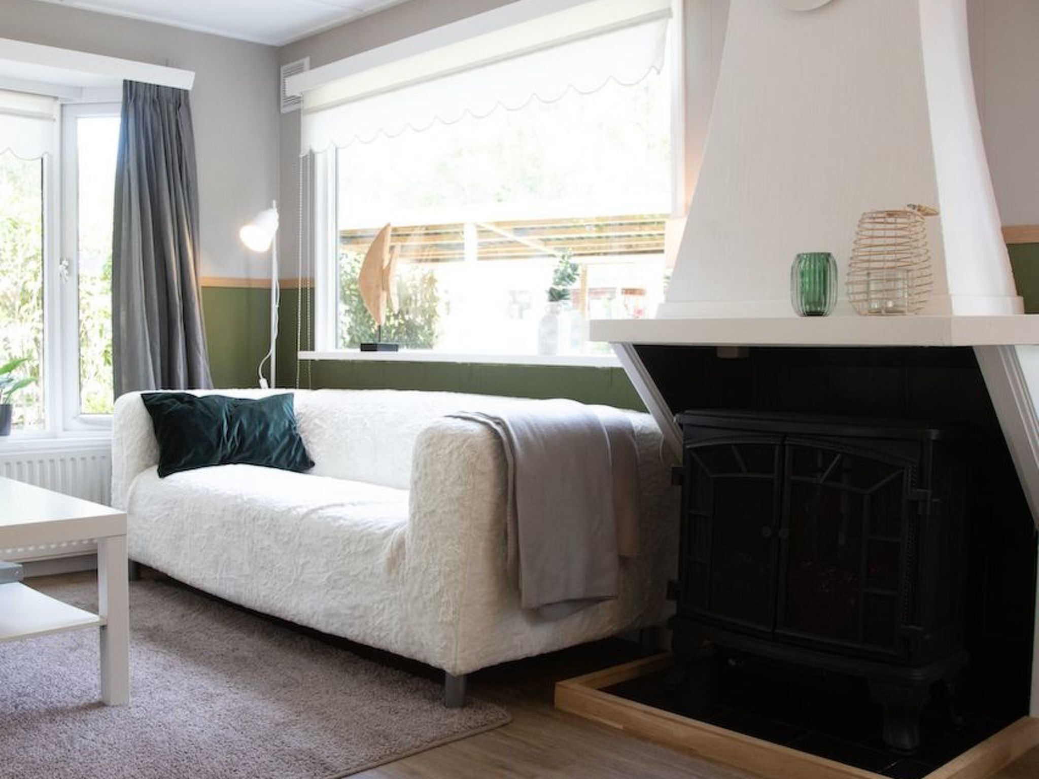 Een gezellige woonkamer met een witte bank, een open haard en uitzicht op de omgeving.