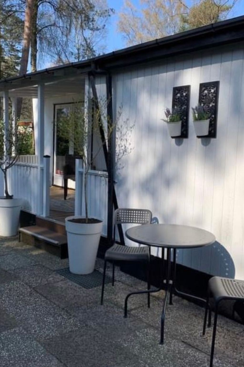 A covered outdoor seating area with a table and chairs, potted plants, and a bench.