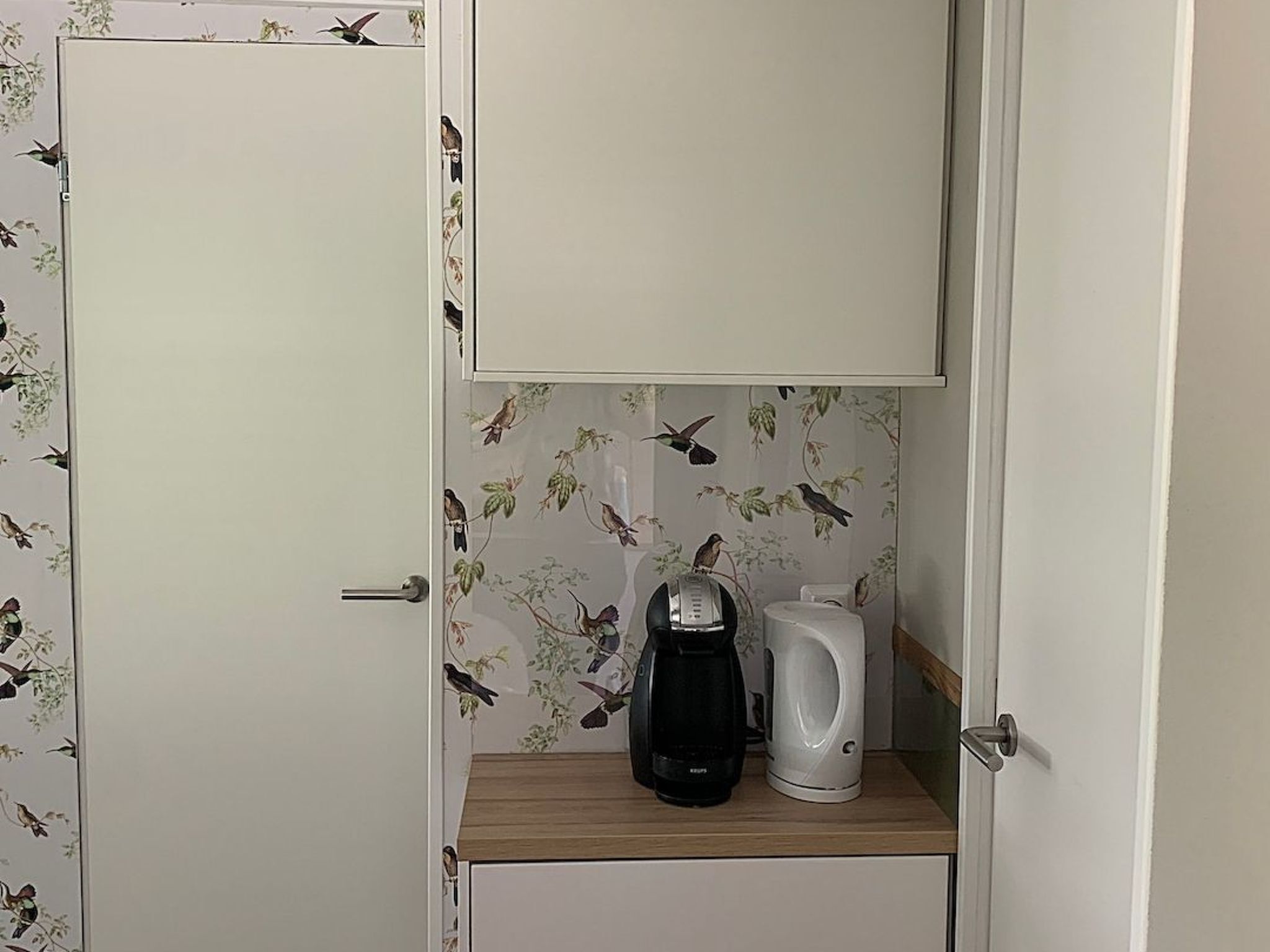 A small kitchenette with a coffee maker and a kettle on a wooden countertop.
