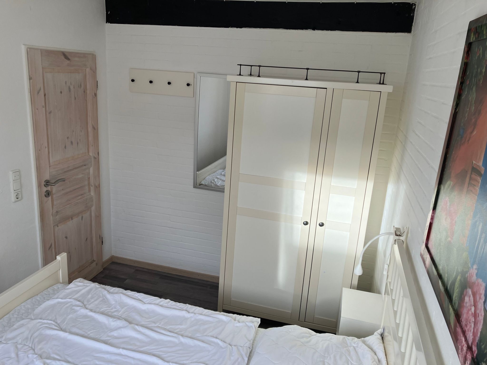 A bedroom with a wooden door, a wardrobe, a bed, and a mirror.