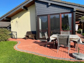 A building with a number 74 sign, a patio with a table and chairs, and a grassy area. - Vacation home 4 J by Interhome (Burhave)