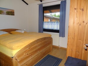 A wooden bed with a yellow bedspread, a window with blue curtains, and a view of a building outside. - Vacation home 4 J by Interhome (Burhave)