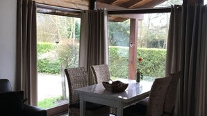 Een eetgedeelte met een tafel en stoelen, een bijzettafeltje en uitzicht op groen buiten.