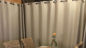 Een eethoek met een tafel en stoelen, een vaas met een bloem, en een gordijnenachtergrond.