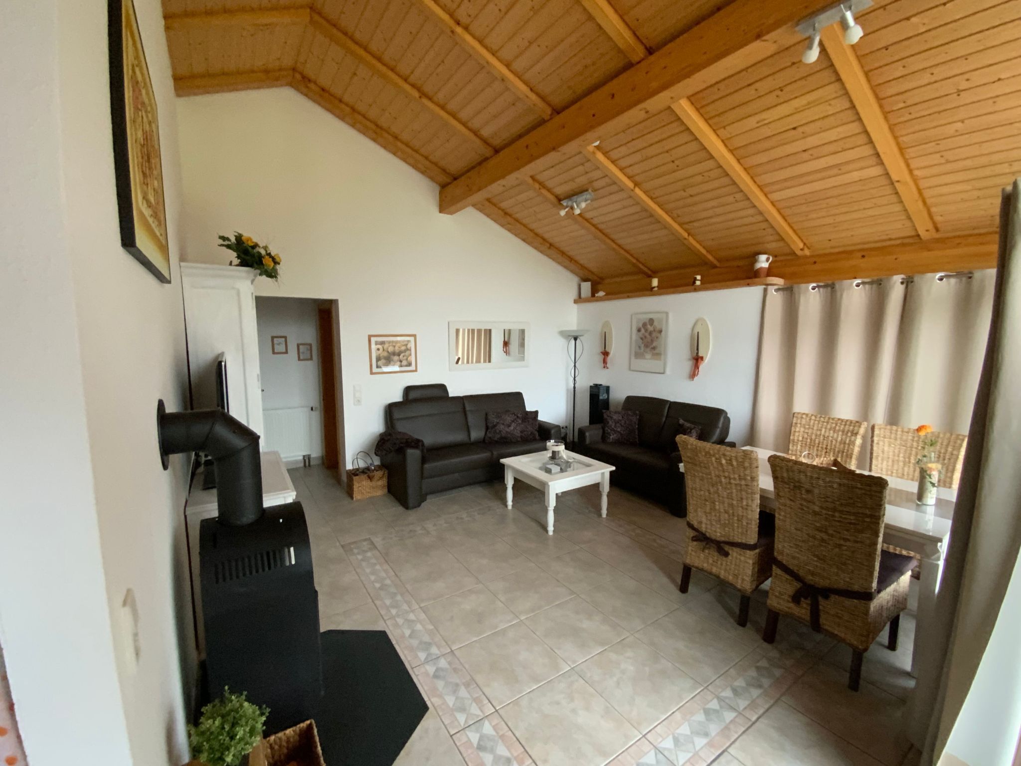 Amplia sala de estar con techo de madera alto, dos sofás, una mesa de centro y sillas de mimbre.