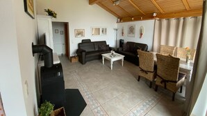 Een ruime woonkamer met een hoog houten plafond, twee banken, een salontafel en rieten stoelen.