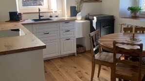 Eine moderne Küche mit Holzboden, weißen Schränken, einem Essbereich mit Holztisch und -stühlen und Blick auf ein Gebäude vor dem Fenster.
