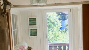 Ein Zimmer mit einem weißen Tisch, einer Bank, einer Topfpflanze und Blick auf einen Balkon mit Holzgeländer.