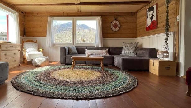 Ein gemütliches Wohnzimmer mit Holzboden, einem großen Fenster, einer Couch, einem Couchtisch und einem Teppich.