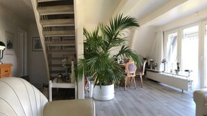 Un vaste salon doté d’un haut plafond, d’un escalier et d’un coin repas avec des chaises et une table en bois.