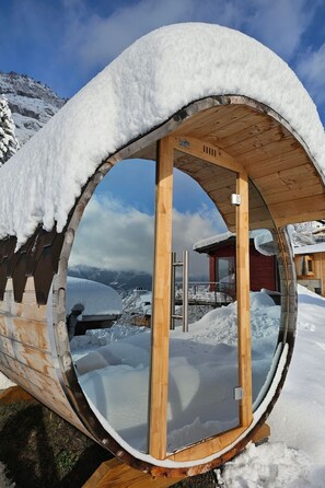 Ein mit Schnee bedecktes Holzgebäude mit rundem Fenster vor einer verschneiten Berglandschaft.