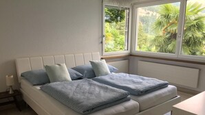 A bedroom with a bed, pillows, a nightstand, and a window with a view of greenery. - Apartment Weggis by Interhome (Weggis)