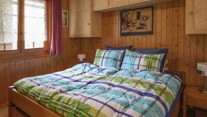 Een kamer met houten lambrisering, een bed, gordijnen voor het raam en een schilderij aan de muur.