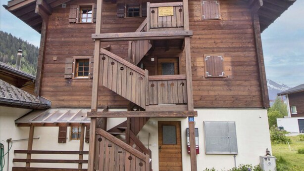 Een houten gebouw met een balkon en een trap naar de ingang.