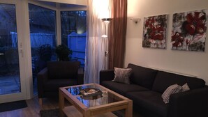 Ein Wohnzimmer mit Glastür zum Patio, einem dunklen Sofa, einem Holztisch und abstrakten floralen Wandbildern.