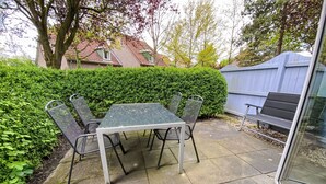 Eine Terrasse mit Tisch und Stühlen, umgeben von einer Hecke und einem blauen Zaun.