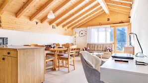 Ett mysigt, väl upplyst rum med ett träpanelat tak, en matplats med stolar och ett bord, en soffa och ett skrivbord med en lampa.