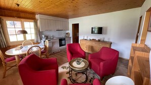 Un salon chaleureux avec des fauteuils rouges, une petite table ronde et un téléviseur fixé au mur.