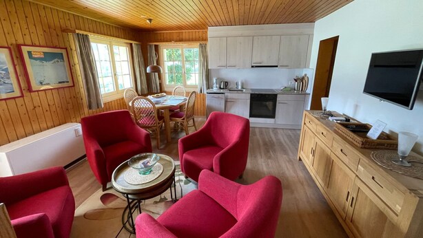 Un intérieur de chalet chaleureux avec un coin repas, une cuisine et un espace détente agrémenté de chaises rouges.