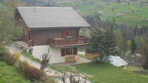 Une maison en bois dotée d’un balcon, entourée de verdure et située dans un paysage montagneux.