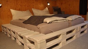 A bed with a wooden frame and a headboard made of wooden pallets, set in a room with wooden walls and a carpeted floor. - Chalet 9 by Interhome (Innertkirchen)