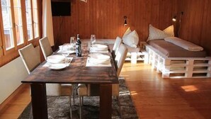 A wooden interior with a dining table set for four, a sofa, and a TV mounted on the wall. - Chalet 9 by Interhome (Innertkirchen)