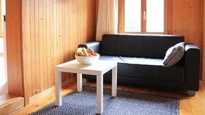 A cozy room with a wooden wall, a black sofa, a small white table, and a bowl of snacks. - Chalet 9 by Interhome (Innertkirchen)