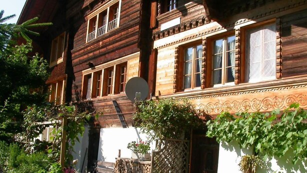 A wooden house with a balcony, a satellite dish, and a garden with plants and a wooden fence. - Darioli by Interhome (Innertkirchen)
