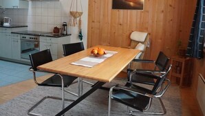 A modern kitchen with a wooden interior, a dining table with chairs, and a hanging light fixture. - Darioli by Interhome (Innertkirchen)