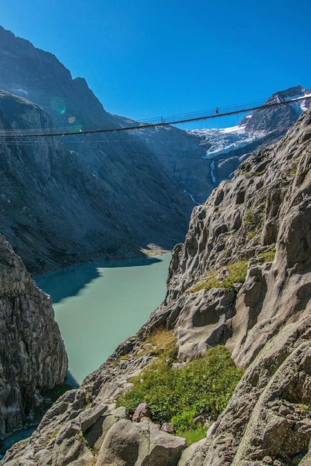 Uma ponte suspensa sobre um cânion profundo, com um lago abaixo.